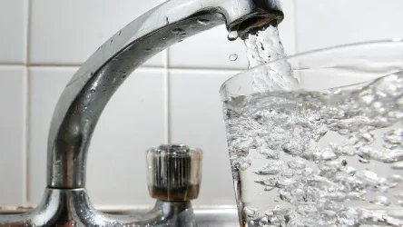 A glass is being filled with water from a running kitchen tap, with clear bubbles visible in the water.